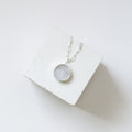 Round moonstone pendant on a silver chain draped over a white cube.