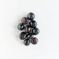 A bunch of dark red, tumbled garnet stones on a white background.
