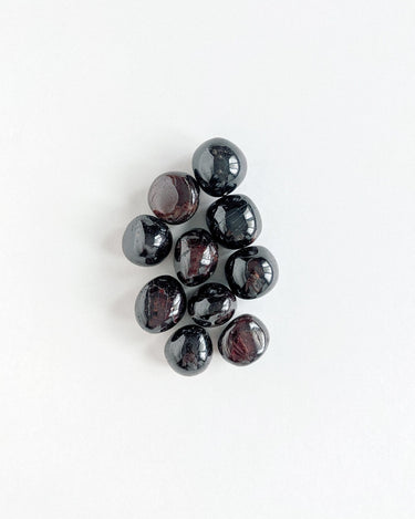 A bunch of dark red, tumbled garnet stones on a white background.