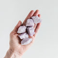 A bunch of soft purple, rough Kunzite stones held on a hand.